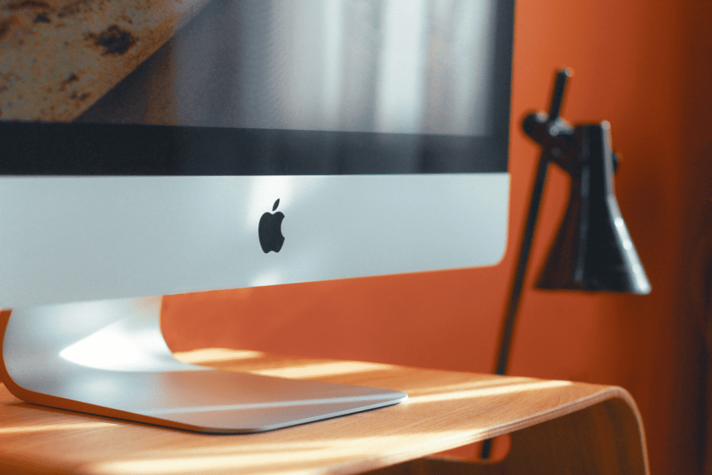 Apple computer screen on a desk with a lamp in the background.