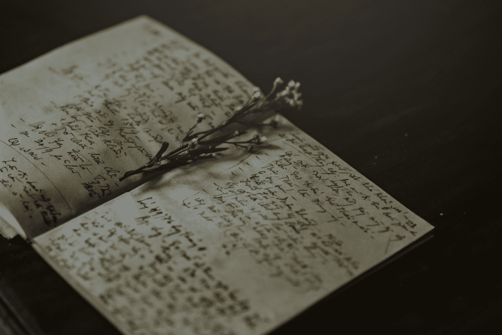 Dried flowers lying in an open book on a table. The book looks like a diary with handwritten notes.