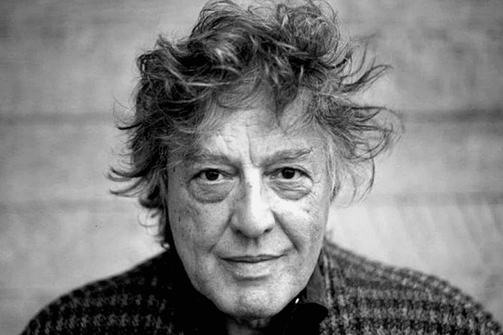 Tom Stoppard. Black and white head and shoulders photo of a older man with messy hair looking at the camera.