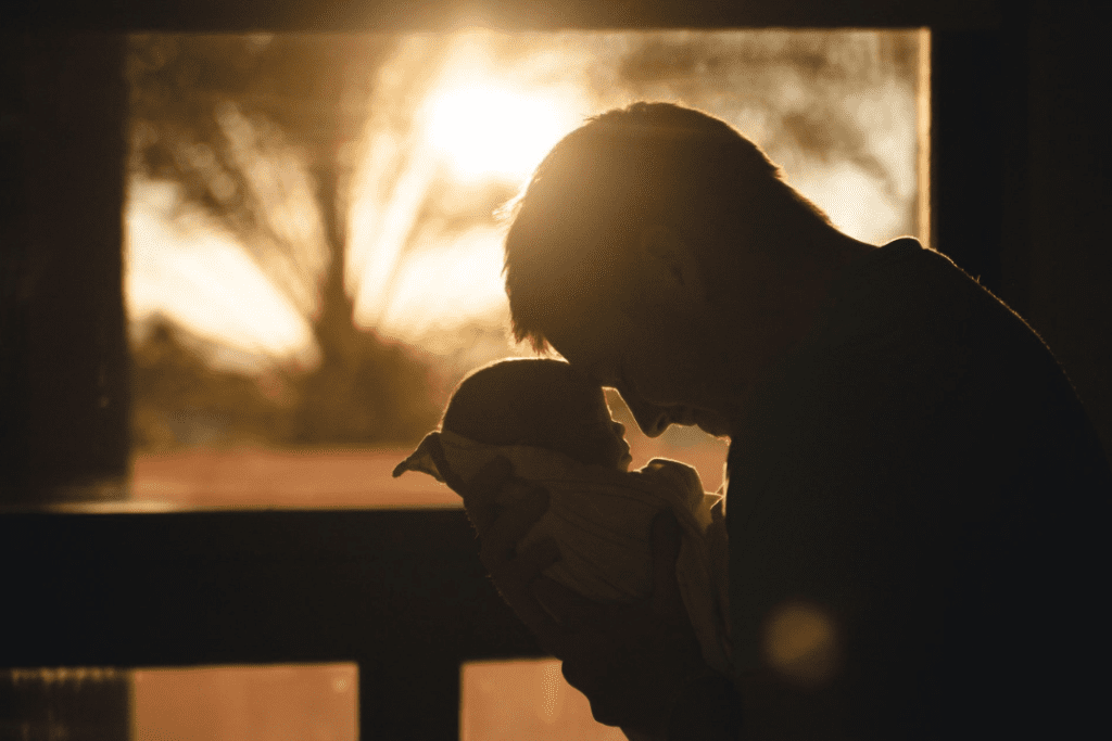 Silhouette of a man and newborn baby touching foreheads. The man is holding the baby.