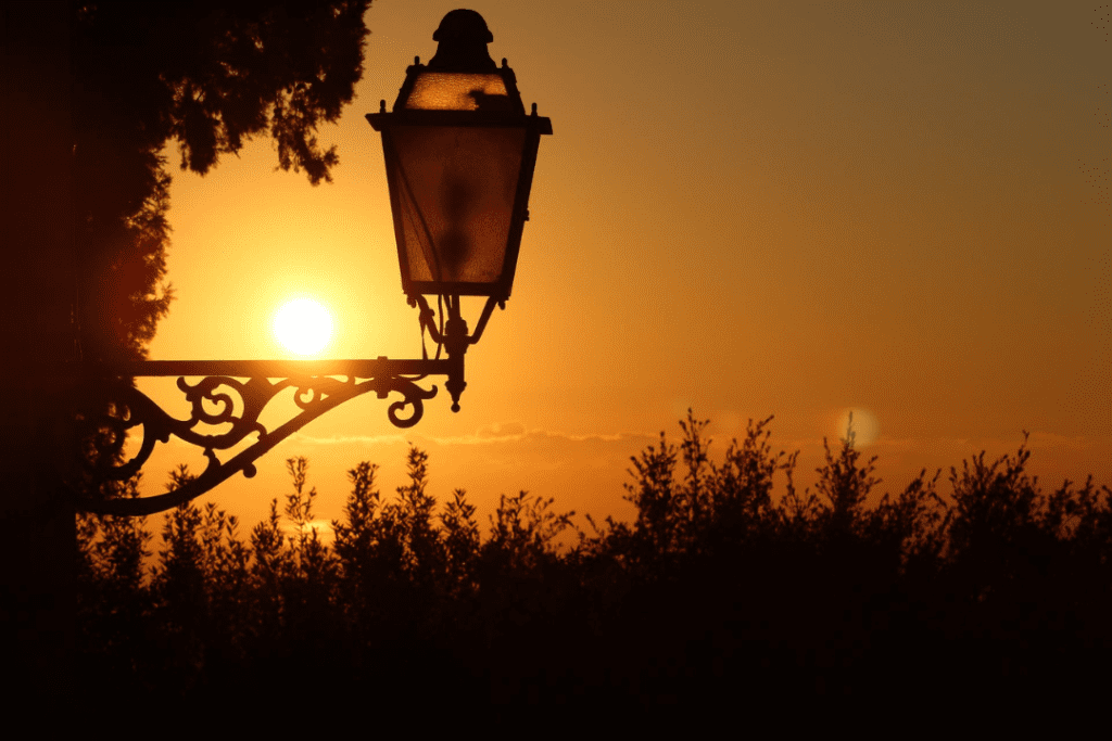 A decorative lamp post attached to a wall silhouetted against a golden sky.