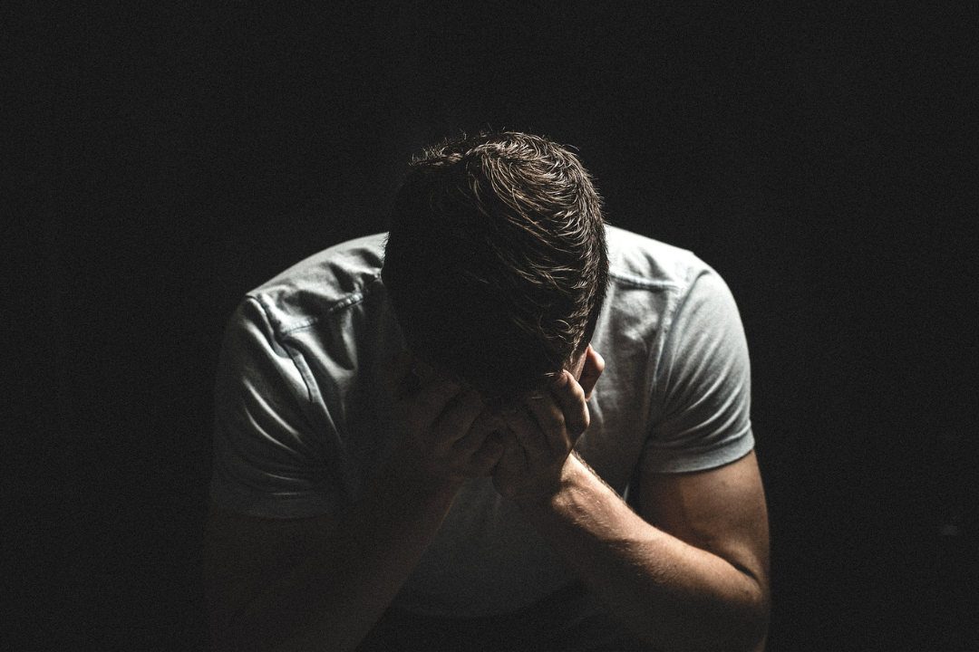 Man in a tshirt sitting with his head in his hands.