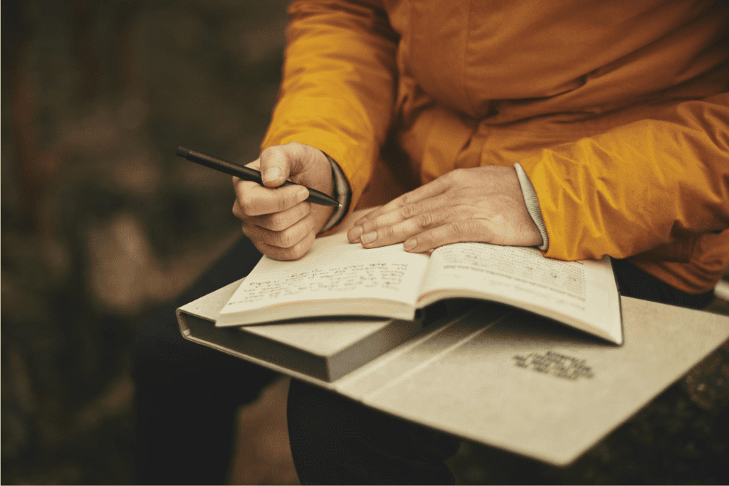 A person wearing a yellow jacket is sitting writing in a journal.