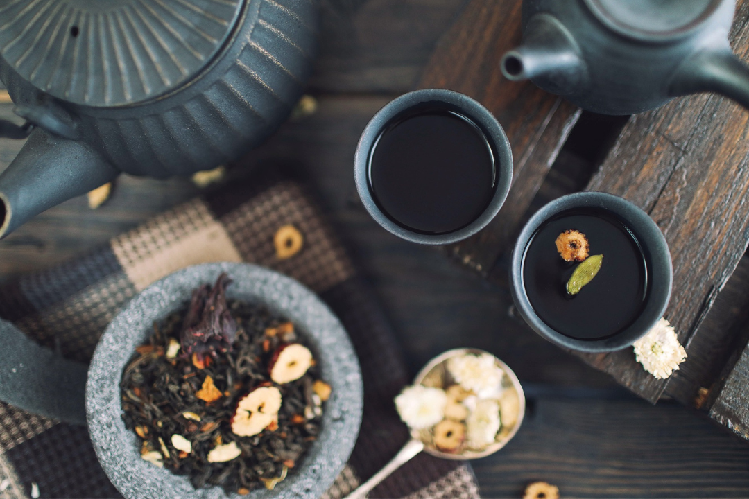 The camera is looking down on a table with looseleaf tea, a teapot and teacups filled with tea.