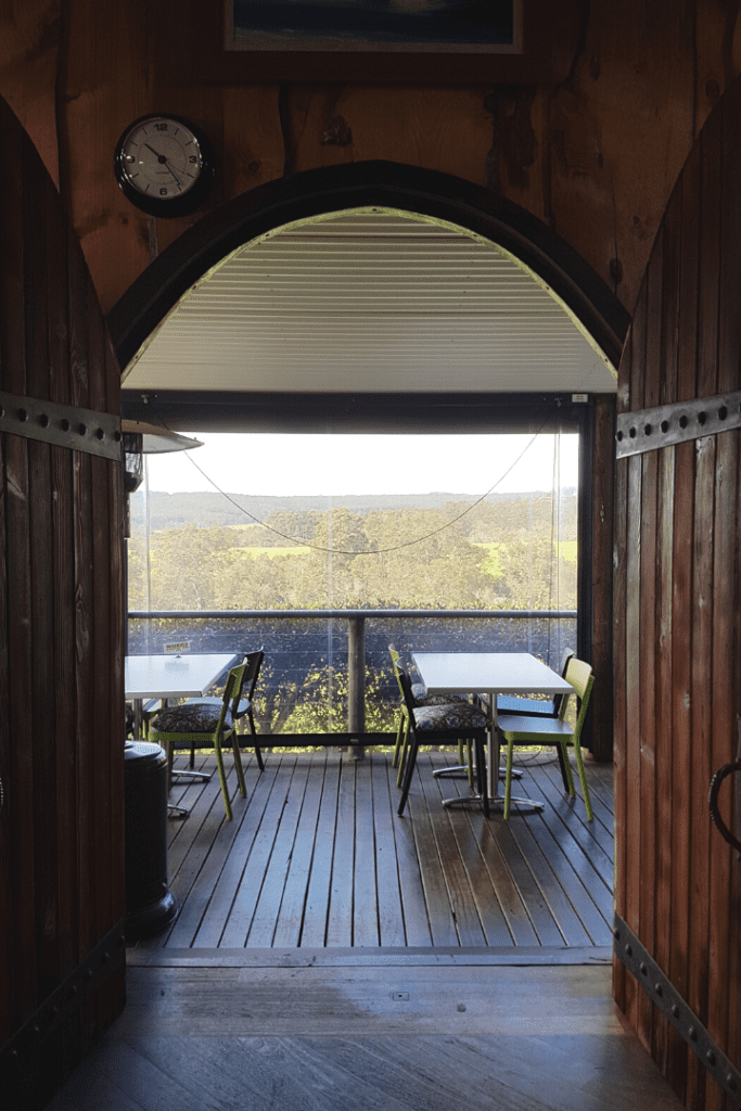 View through a doorway to a balcony with tables. Trees and hills in the background.