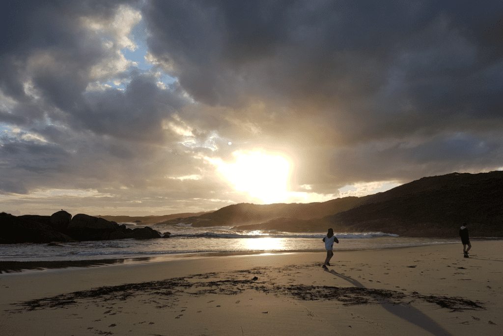 Older children running on a beach on a cloudy beach at sunset