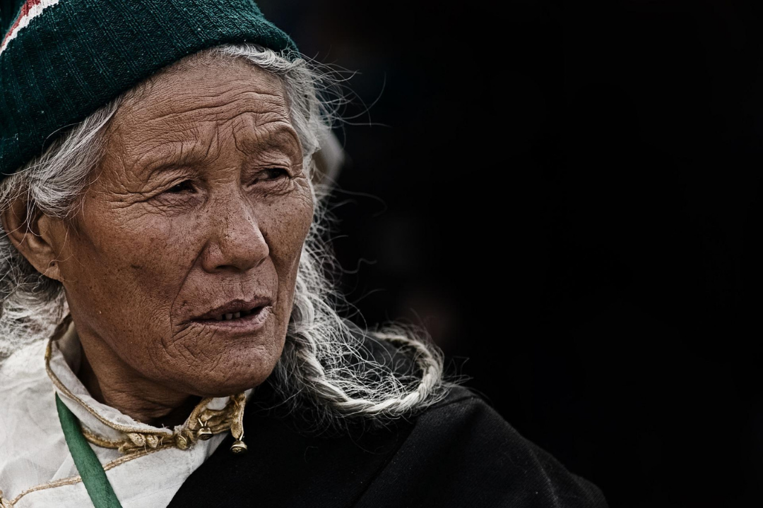 Elderly senior female with a grey plait, wearing a beanie.