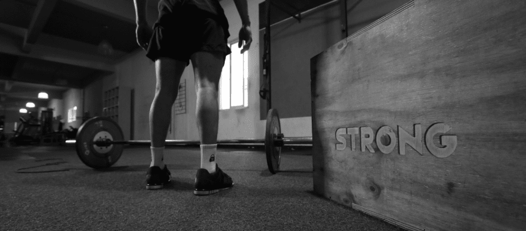 Man in a gym standing in front of a barbell on the ground.